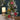 Small decorated Christmas tree with hanging ornaments and a candle in the background